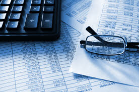 Tax paperwork on a desk under keyboard and glasses