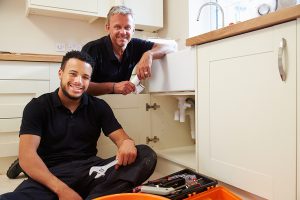 Plumber and apprentice repairing kitchen