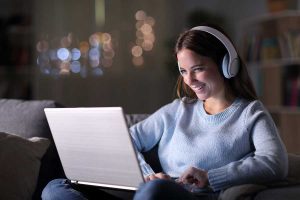 Young woman with headphones on smiling at her laptop