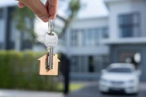 Keys to an investment property with a house in the background and a car parked