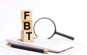 Fringe benefits tax (FBT) blocks with magnifying glass and notepad