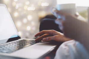 Close up of a person using a laptop and holding a mug