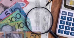 Australian dollars on a table with a magnifying glass. Budget 2026-27 WATO